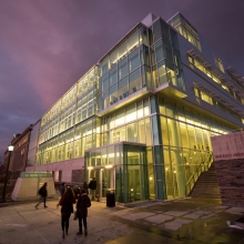 The glass facade of the Physical Sciences Building lit up in the evening.